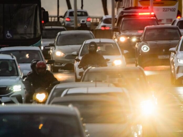 Trânsito de veículos em avenida de Brasília ao entardecer, com carros e motos