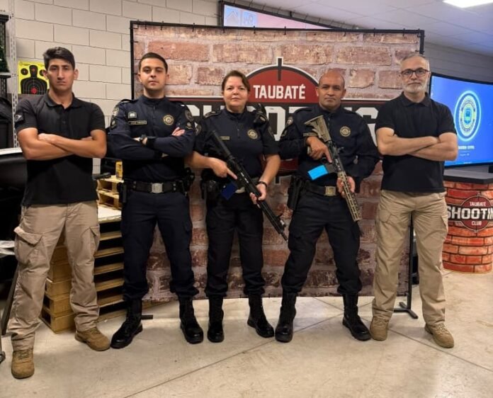 Cinco pessoas posam diante de painel do Taubaté Shooting Club, em capacitação com simulador virtual de tiro